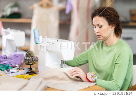 Female tailor using sewing machine to make garment in studio 129195614