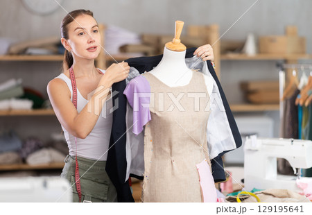 Young tailoress trying ready jacket on mannequin Young tailoress trying ready jacket on mannequin 129195641