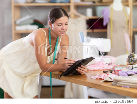 Female tailor create sketch of dress in tablet 129195664
