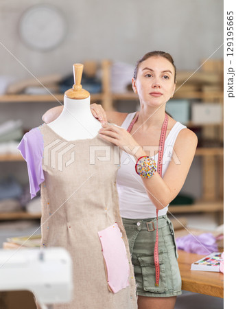 dressmaker works on a dress near a mannequin dressmaker works on a dress near a mannequin 129195665
