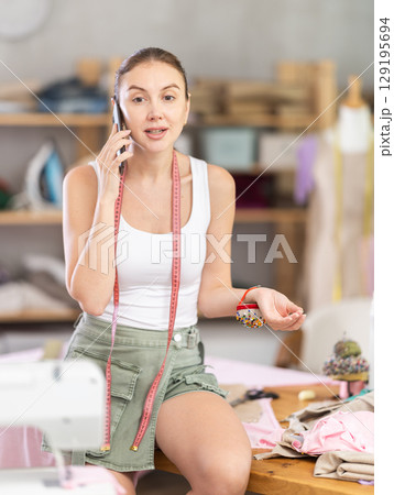 Woman seamstress talks on phone in workshop 129195694