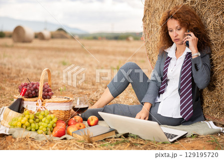 Woman in office clothes talking on mobile phone at picnic in field Woman in office clothes talking on mobile phone at picnic in field 129195720