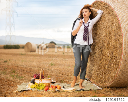 Young woman in white blouse and gray business suit standing on soft plaid mat near stack of straw Young woman in white blouse and gray business suit standing on soft plaid mat near stack of straw 129195722