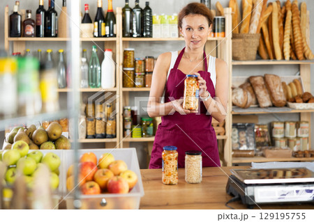 Friendly female seller offers to buy canned beans in interior of grocery supermarket 129195755