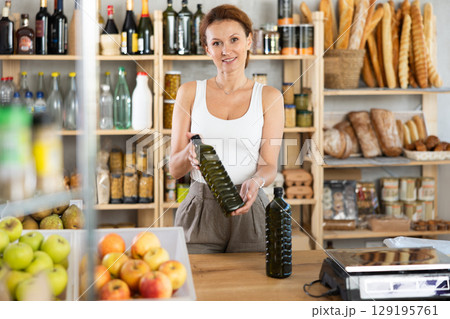 Adult woman seller offering olive oil in grocery Adult woman seller offering olive oil in grocery 129195761