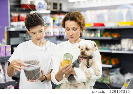 Woman with teenage son choosing food for Yorkshire terrier in pet store 129195859