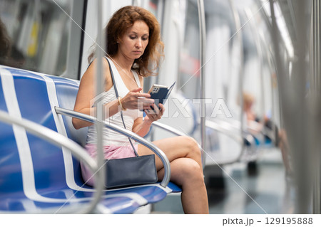 Adult woman sitting in subway car with phone Adult woman sitting in subway car with phone 129195888