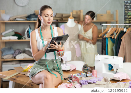 Female tailor create sketch of dress on tablet. Assistant work with mannequin in background 129195932