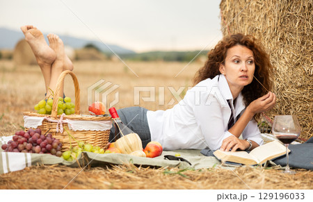 Woman in white blouse spends time in field, settled down in nature with book. 129196033