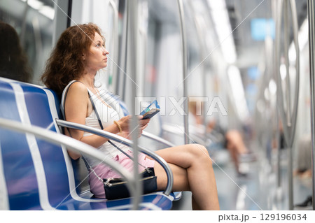 Adult woman sitting in subway car with phone 129196034