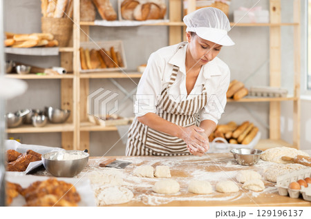 Adult woman baker molding pieces of dough Adult woman baker molding pieces of dough 129196137