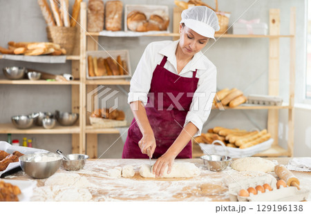 Skilled female baker slicing dough in artisan bakery Skilled female baker slicing dough in artisan bakery 129196138