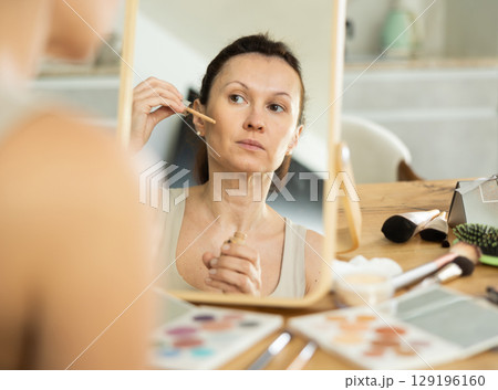 Woman applying cosmetic foundation on facial skin in front of mirror Woman applying cosmetic foundation on facial skin in front of mirror 129196160