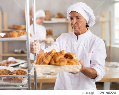 Elderly woman baker with basket of croissants 129196228