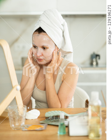 Woman with towel head wrap applying cosmetic face mask Woman with towel head wrap applying cosmetic face mask 129196271