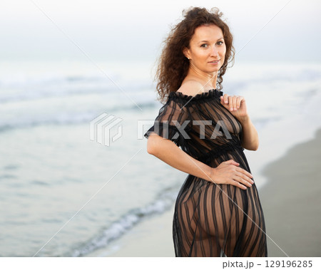 Back view of woman in black peignoir standing on coast 129196285