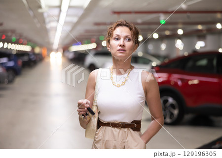 Adult woman stands in parking lot with keys 129196305