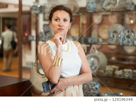 Woman with piece of paper and phone in hands walks around museum hall, view exhibition 129196349