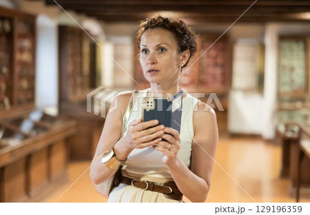 Woman takes pictures of exhibits in glass cases at history museum using her smartphone 129196359