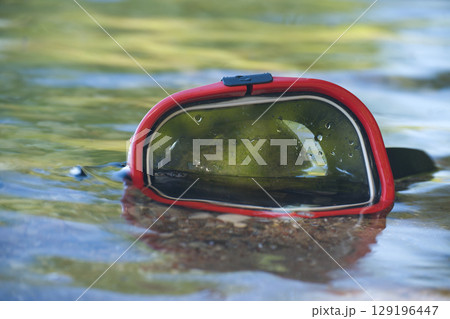 Snorkeling mask resting on the surface of a clear, shallow body of water. 129196447