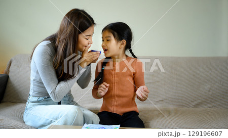 Happy mom and daughter enjoying a beauty care routine together in a living room Happy mom and daughter enjoying a beauty care routine together in a living room 129196607