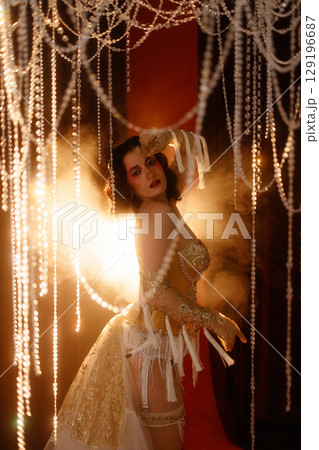 Circus-inspired retro burlesque dancer posing in golden corset with theatrical decor 129196687