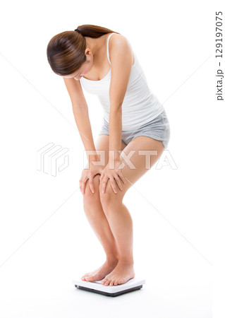 体重計に乗り体重をはかる若い女性. 129197075