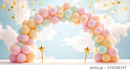 A colorful balloon arch in pastel shades of pink, blue, and yellow. The background features a bright sky with fluffy clouds and golden stars hanging above. 129198147