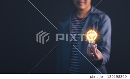 New generation businesswoman holding a glowing light bulb in a dark background, symbolizing creativity, innovation, and bright ideas. Business global internet connection application technology. 129198260