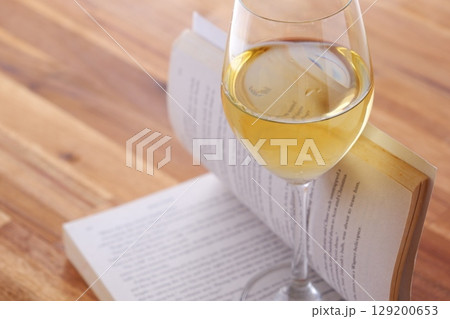 ワインのグラスと本 - 白ワインを飲みながら読書を楽しんでいるイメージ 129200653
