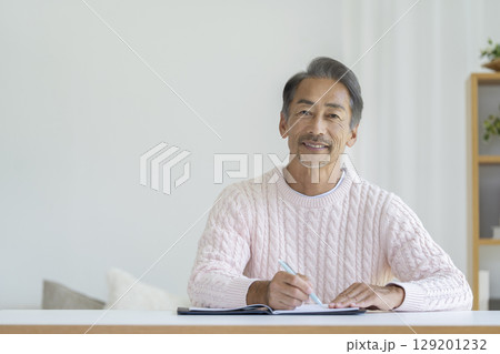 ペンを持って微笑むカメラ目線のシニア男性 129201232