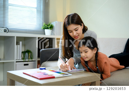 Loving mother helping daughter with homework or art project in a bright living room 129201653