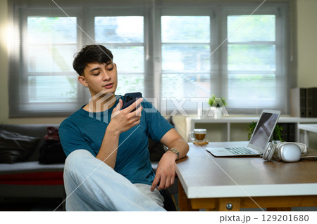 Happy young caucasian man using smartphone in home office Happy young caucasian man using smartphone in home office 129201680