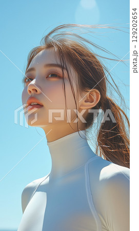 Young Korean woman with ponytail enjoys a sunny day at the beach, showcasing a serene expression and clear blue sky 129202654
