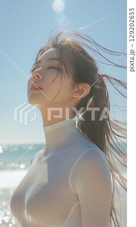 Young woman enjoying the beach breeze while standing by the ocean under a clear blue sky on a sunny day 129202655
