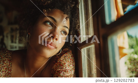 A contemplative young woman looking out her home window, daydreaming. A contemplative young woman looking out her home window, daydreaming. 129202783