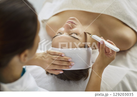 Closeup of beautician hands making facial cleaning procedure on woman client face in spa salon. 129203035