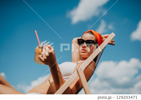 Young woman sitting by swimming pool and drinking limonade. 129203471