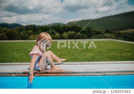 Child sitting by the poolside and playing. 129203483