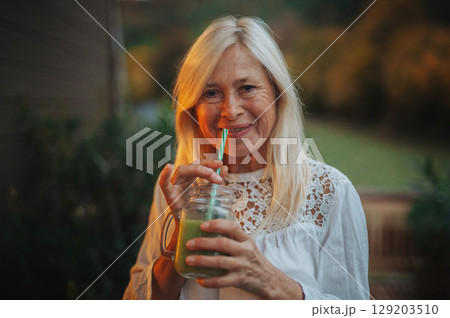 Smiling senior woman drinking green smoothie outdoors 129203510