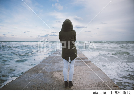 Woman stands on a pier looking out at the ocean Woman stands on a pier looking out at the ocean 129203617
