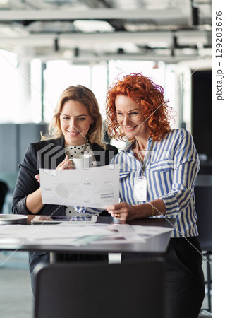 Two female colleagues analyzing project documents in modern office. 129203676