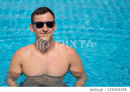 Young man relaxing in swimming pool wearing sunglasses 129204389