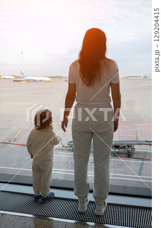 Mother and child watching airplane taking off from airport window Mother and child watching airplane taking off from airport window 129204415