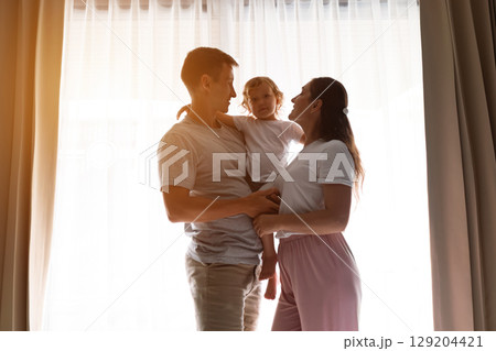 Happy family embracing near window in morning light 129204421