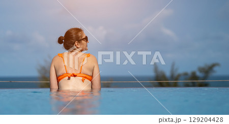 Tourist relaxing in infinity pool enjoying ocean view Tourist relaxing in infinity pool enjoying ocean view 129204428