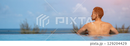 Tourist relaxing in infinity pool overlooking tropical ocean 129204429