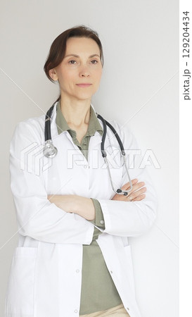 Female medical professional in white lab coat, stethoscope draped, standing with crossed arms and displaying confident, authoritative healthcare demeanor. Medicine and health care Female medical professional in white lab coat, stethoscope draped, standing with crossed arms and displaying confident, authoritative healthcare demeanor. Medicine and health care 129204434