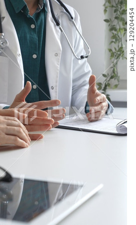 Doctor man wearing medical coat over green shirt, and stethoscope is gesturing with hands over white table while explaining diagnosis to patient. Medicine and health care concept 129204454