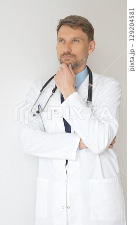 Portrait of a confident male doctor wearing stethoscope and white coat, standing with crossed arms and gazing thoughtfully, representing medical professionalism and expertise Portrait of a confident male doctor wearing stethoscope and white coat, standing with crossed arms and gazing thoughtfully, representing medical professionalism and expertise 129204581